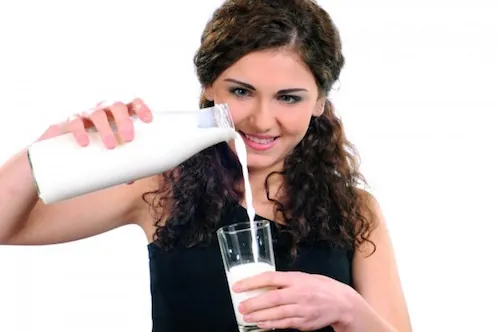 Femme souriante versant du lait dans un verre.