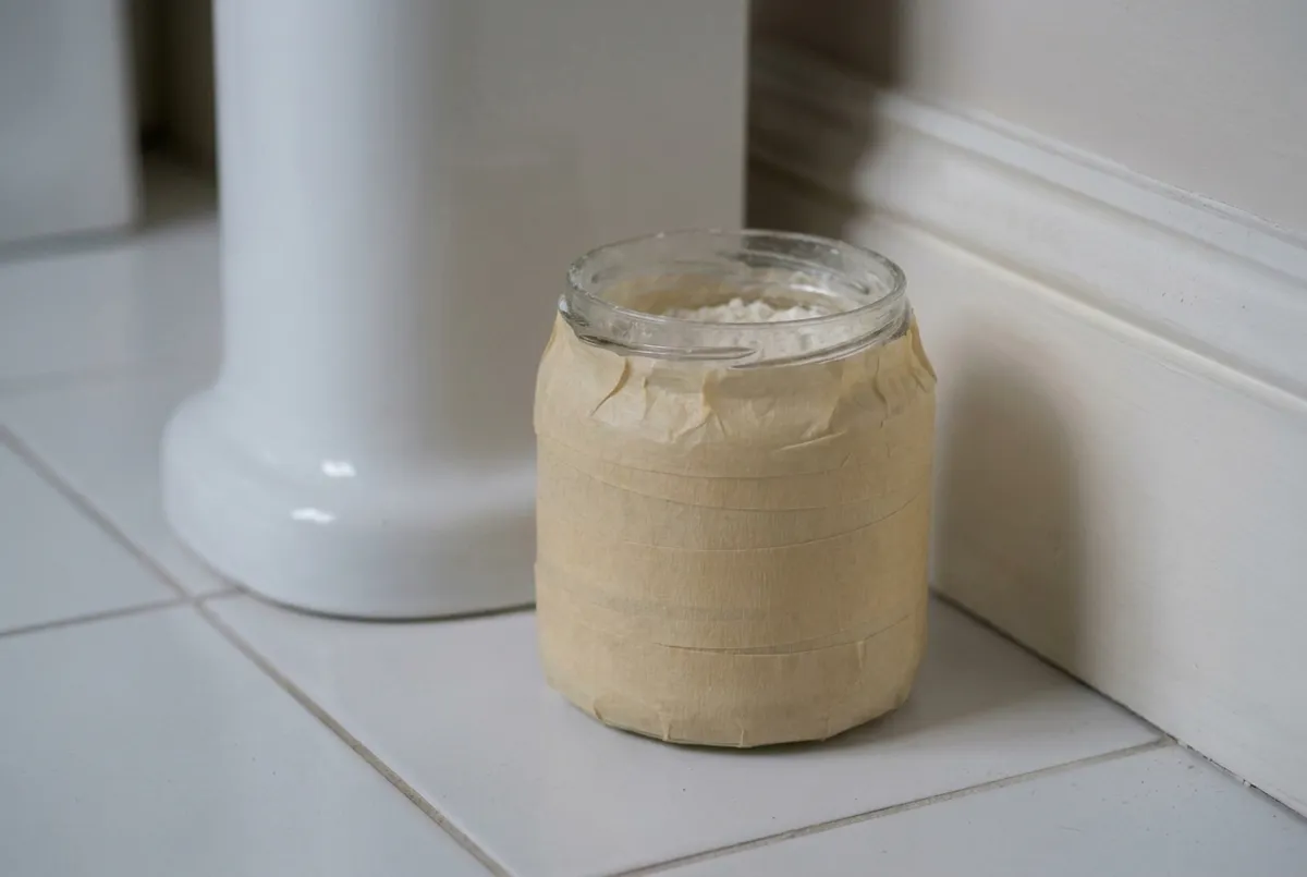 Piège à poissons d'argent : petit pot en verre entouré de ruban de masquage, une pincée de farine au fond, posé au pied d'un lavabo
