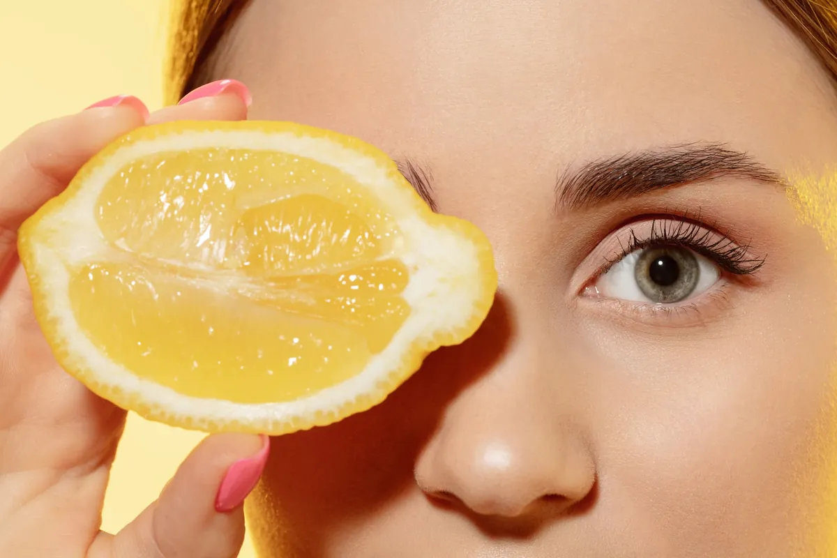 Femme tenant un citron frais près de son visage.